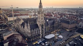 Luftaufnahme des Neuen Rathauses in München bei Sonnenuntergang, umgeben von städtischen Gebäuden und einem offenen Platz.