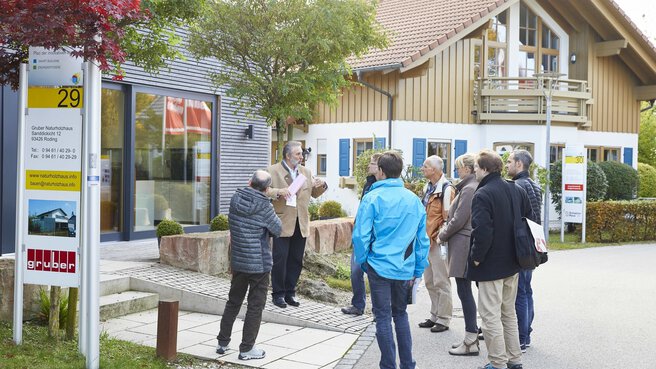 Menschen, die im Freien im Bauzentrum Poing stehen und dem Vortrag zu einem Musterhaus lauschen.