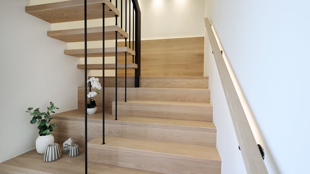 Ein helles beleuchtetes Treppenhaus mit Holzstufen und einem Absatz auf der Hälfte der Höhe.