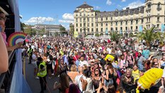 Große Menschenmenge bei einem Fest im Freien, mit tanzenden Menschen und bunten Luftballons unter einem sonnigen Himmel.