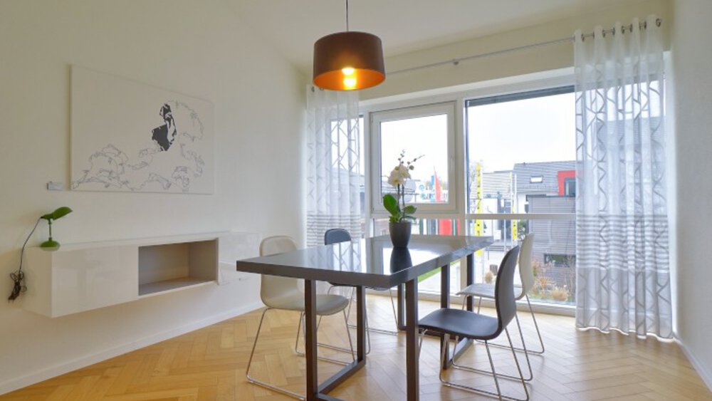 Modernes Esszimmer mit einem dunklen Tisch, vier Stühlen und einem großen Fenster mit transparenten Vorhängen, die Tageslicht hereinlassen.