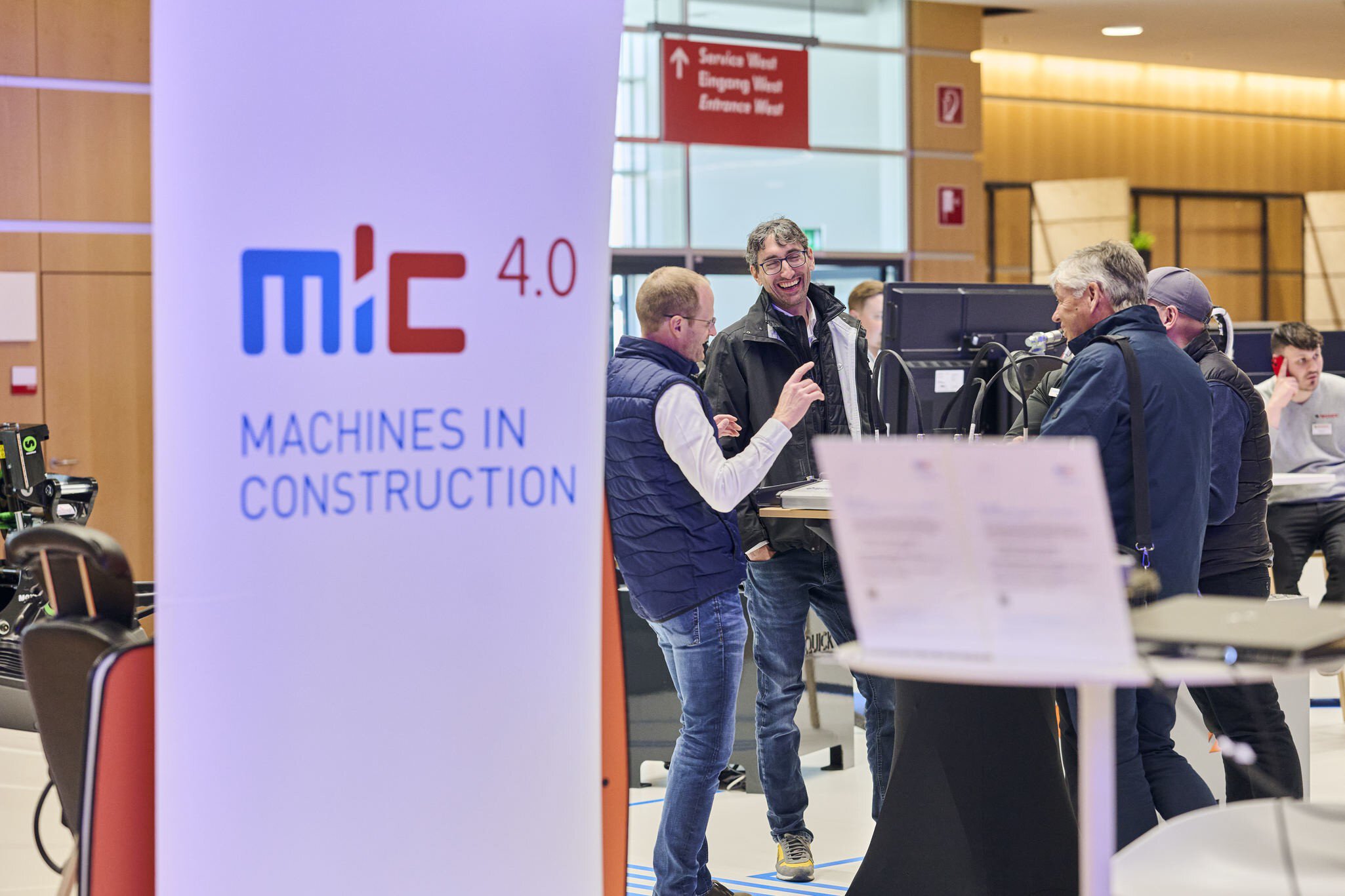 Lachende Messebesucher im Gespräch am Stand von MiC 4.0 – Machines in Construction.