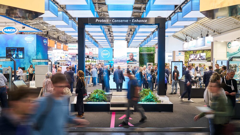 A modern, open-plan trade fair stand under blue and white lighting elements with the slogan 