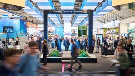 A modern, open-plan trade fair stand under blue and white lighting elements with the slogan 