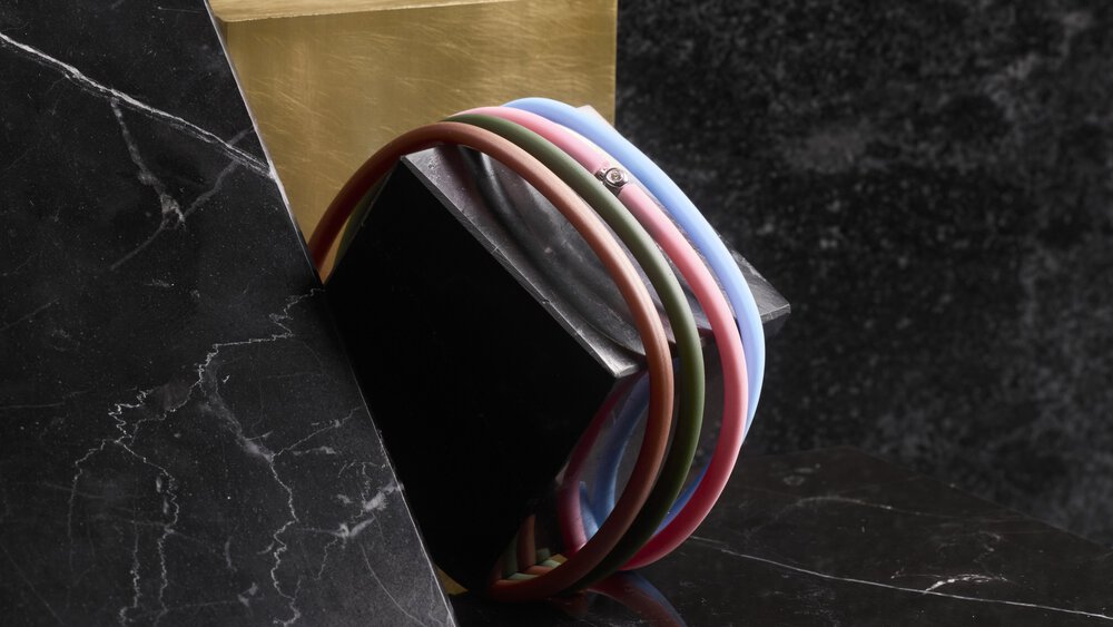 Colourful bracelet consisting of four ribbons wrapped around a black block with a golden background on a dark marble surface.