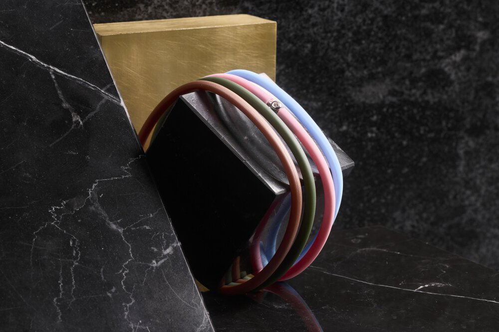 Buntes Armband, bestehend aus vier Bändchen um einen schwarzen Block mit goldenem Hintergrund auf einer dunklen Marmoroberfläche gewickelt.