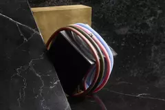 Buntes Armband, bestehend aus vier Bändchen um einen schwarzen Block mit goldenem Hintergrund auf einer dunklen Marmoroberfläche gewickelt.
