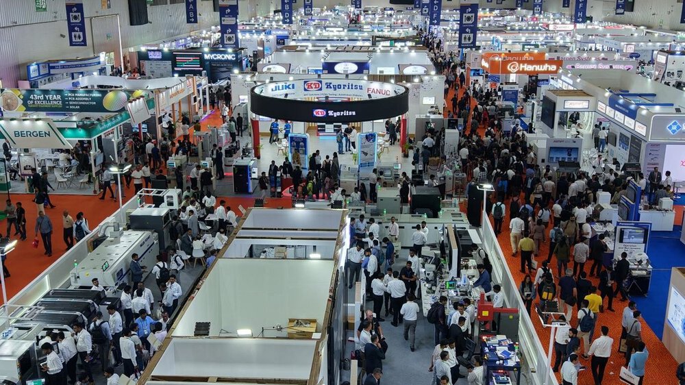 A large covered exhibition hall with many booths, bright lights, and a crowd of people walking around the exhibits.