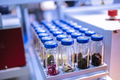 Nahaufnahme eines Analysegeräts: In runden Halterungen sind im Rechteck mehrere Fläschchen mit Aluminium-Septumverschluss (Vials) angeordnet, mit verschiedensten Lebensmittlstückchen bestückt.