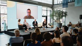 Paneldiskussion beim SZ Nachhaltigkeitsgipfel in München. Auf der Bühne sitzen von rechts nach links Marlene Weiß, Dr. Lisa Irwin-Broß, Rupert Reitberger und Jürgen Reichle. Uwe Ritzer ist per Video auf einer großen Leinwand zugeschaltet.