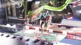 A machine assembles components onto a green printed circuit board in an electronic manufacturing process.