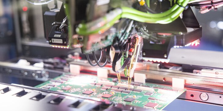 Eine Maschine bestückt eine grüne Leiterplatte mit Bauteilen in einem elektronischen Fertigungsprozess.