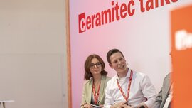 Three people are sitting on a stage beneath the text “ceramitec talks” and looking over at other people outside the picture.