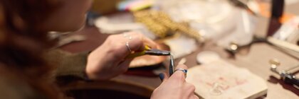 Eine Frau benutzt zwei Zangen, um ein Kettenglied für ein Armband herzustellen.