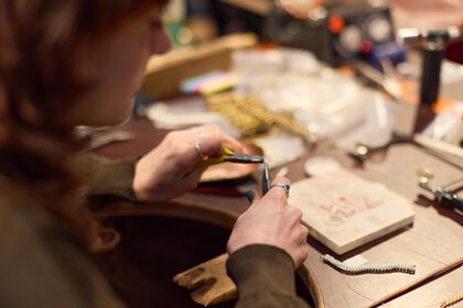 A woman uses two pliers to make a chain link for a bracelet.