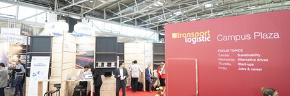 Several exhibitor stands on the Campus Plaza at transport logistic. Some people stand and sit together.