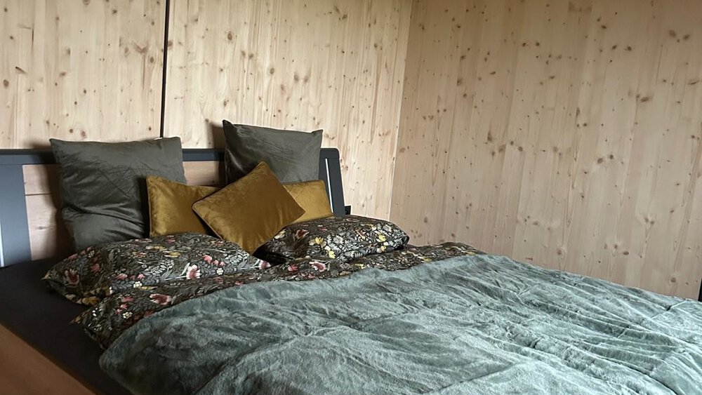 Gemütliches Schlafzimmer aus Holz mit ordentlich gemachtem Bett, grüner Bettwäsche und dekorativen Kissen.