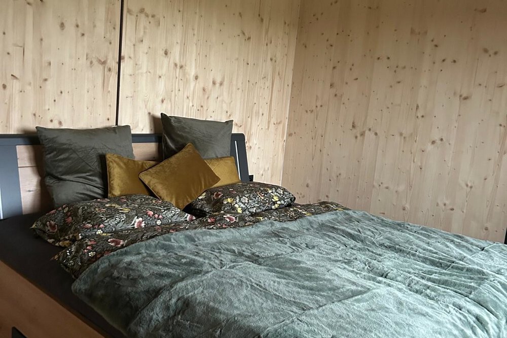 Gemütliches Schlafzimmer aus Holz mit ordentlich gemachtem Bett, grüner Bettwäsche und dekorativen Kissen.