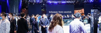 Zahlreiche Besucher auf der AUTO SHANGHAI Messe stehen auf einer Präsentationsfläche voller Autos und mit großen Leinwänden im Hintergrund.