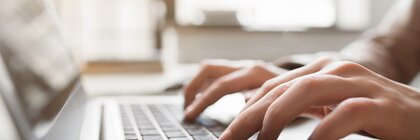 Hände tippen auf einer Laptoptastatur mit unscharfem Hintergrund.
