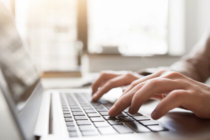 Hands typing on a laptop keyboard with blurred background.