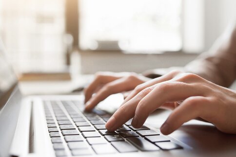 Hands typing on a laptop keyboard with blurred background.