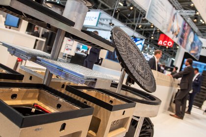 Manhole covers in various shapes, prominently displayed at an exhibition stand. Visitors can be seen in the background.