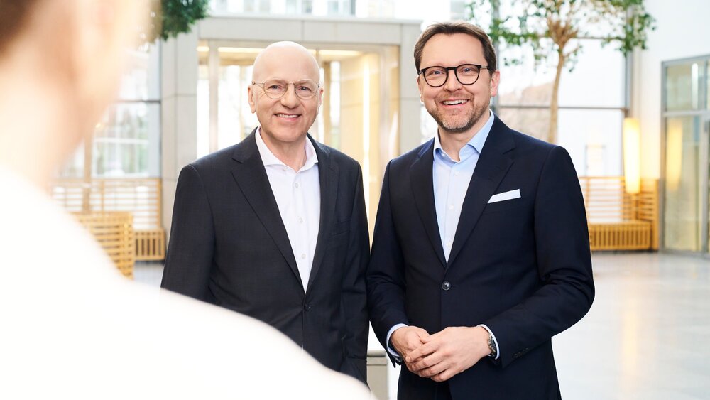 The photo shows two gentlemen, the CEOs of Messe München, both wearing black suits.