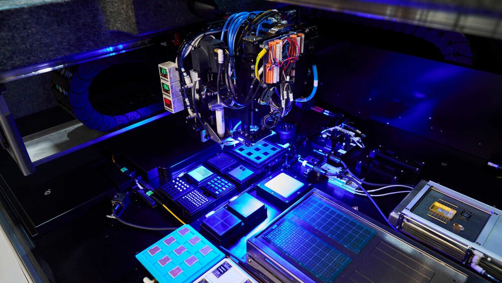 A look inside a blue-lit machine with numerous square circuit boards and a robotic arm hovering above it.