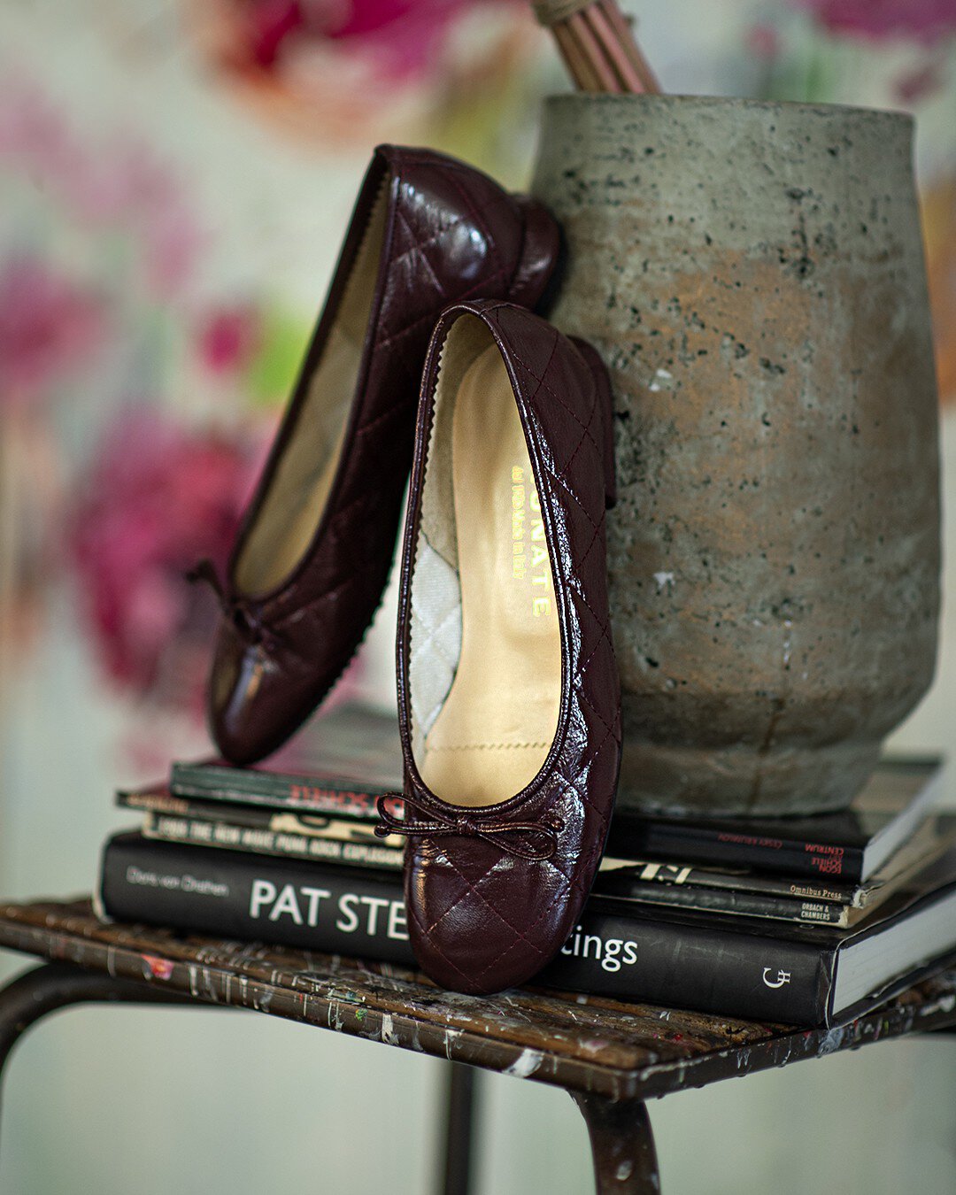Zwei braune Ballerina-Schuhe lehnen dekorativ an einer Vase, die auf einem Stapel Bücher und Hefte steht.