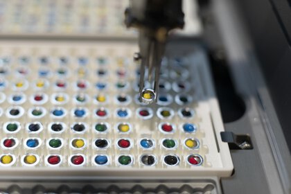 A close-up of a robotic arm selecting a vial from a row of colorful vials in a laboratory automation setup.