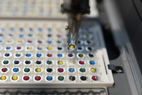 Ein Nahaufnahme eines robotischen Arms, der eine Vial aus einer Reihe bunter Vials in einem Laborautomatisierungsaufbau auswählt.