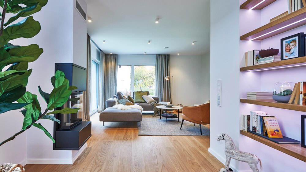 Modernes Wohnzimmer mit Holzboden, großen Fenstern, Grünpflanzen, Bücherregalen und gemütlichen Sitzgelegenheiten.