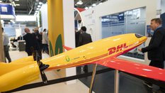 Yellow and red model aeroplane at a trade fair stand at transport logistic, some visitors in the background out of focus.