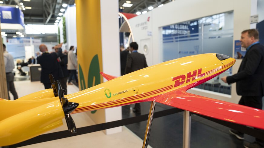 Yellow and red model aeroplane at a trade fair stand at transport logistic, some visitors in the background out of focus.