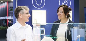 Two people talking at a stand displaying glass and optical components at a modern technology exhibition.