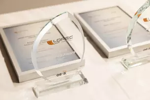 Two glass trophies of the LOPEC Award on a table next to the corresponding framed certificates.