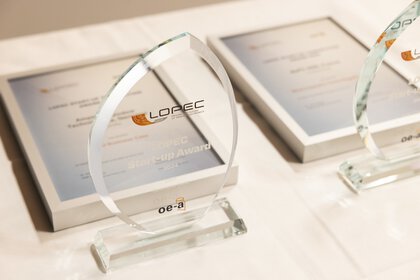 Zwei Glastrophäen des LOPEC Awards auf einem Tisch neben den dazugehörigen, eingerahmten Urkunden.
