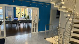 Modernes Büro mit einer blauen Akzentwand, Glastüren, einem Konferenztisch und einer Treppe mit Metallgeländer.