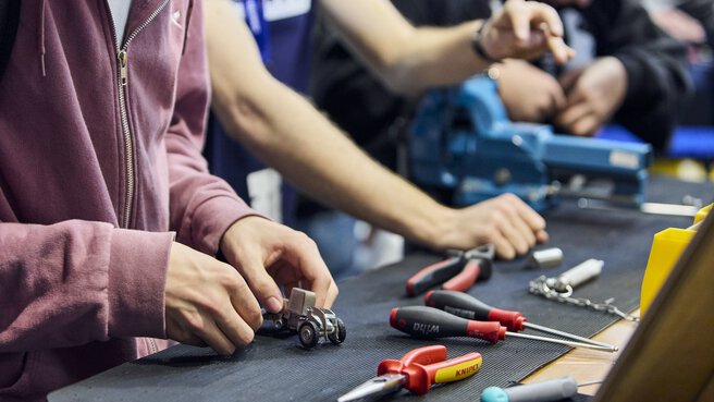 People work with tools on a small model vehicle