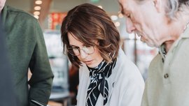 Two men and a woman are standing around a table with tablets in their hands, examining the watches on display.