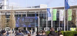 Eingang Nord der Koelnmesse mit Fahnen der digitalBAU. Menschen gehen auf den Messeeingang.