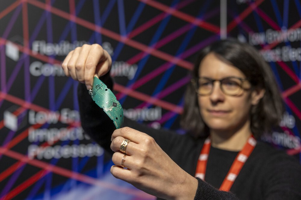A woman holds and bends a flexible green circuit board at LOPEC
