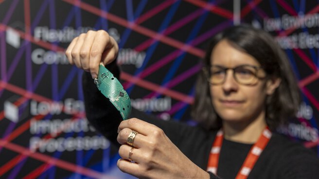 A woman holds and bends a flexible green circuit board at a technology event.