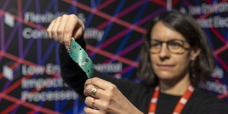 A woman holds and bends a flexible green circuit board at a technology event.