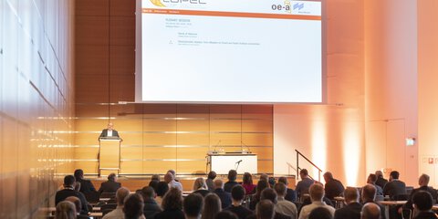 People are sitting in a conference room in front of a presentation screen and the room is illuminated by warm light.