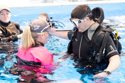 Frau erklärt Mann Taucherequipment im Swimming Pool.