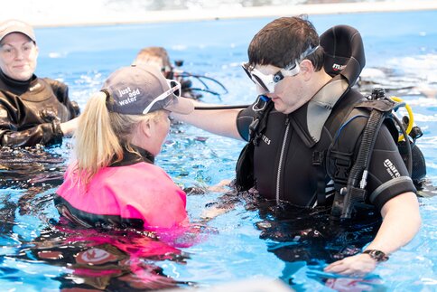 Frau erklärt Mann Taucherequipment im Swimming Pool.