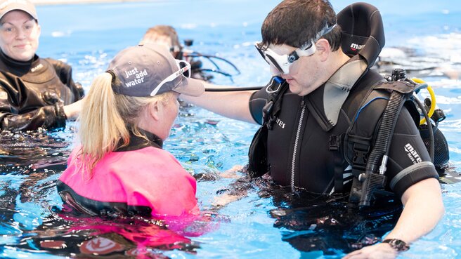 Frau erklärt Mann Taucherequipment im Swimming Pool.