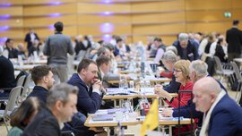 Participants of the bauma Mediendialog 2025 engage in lively discussions at tables in a spacious conference hall.